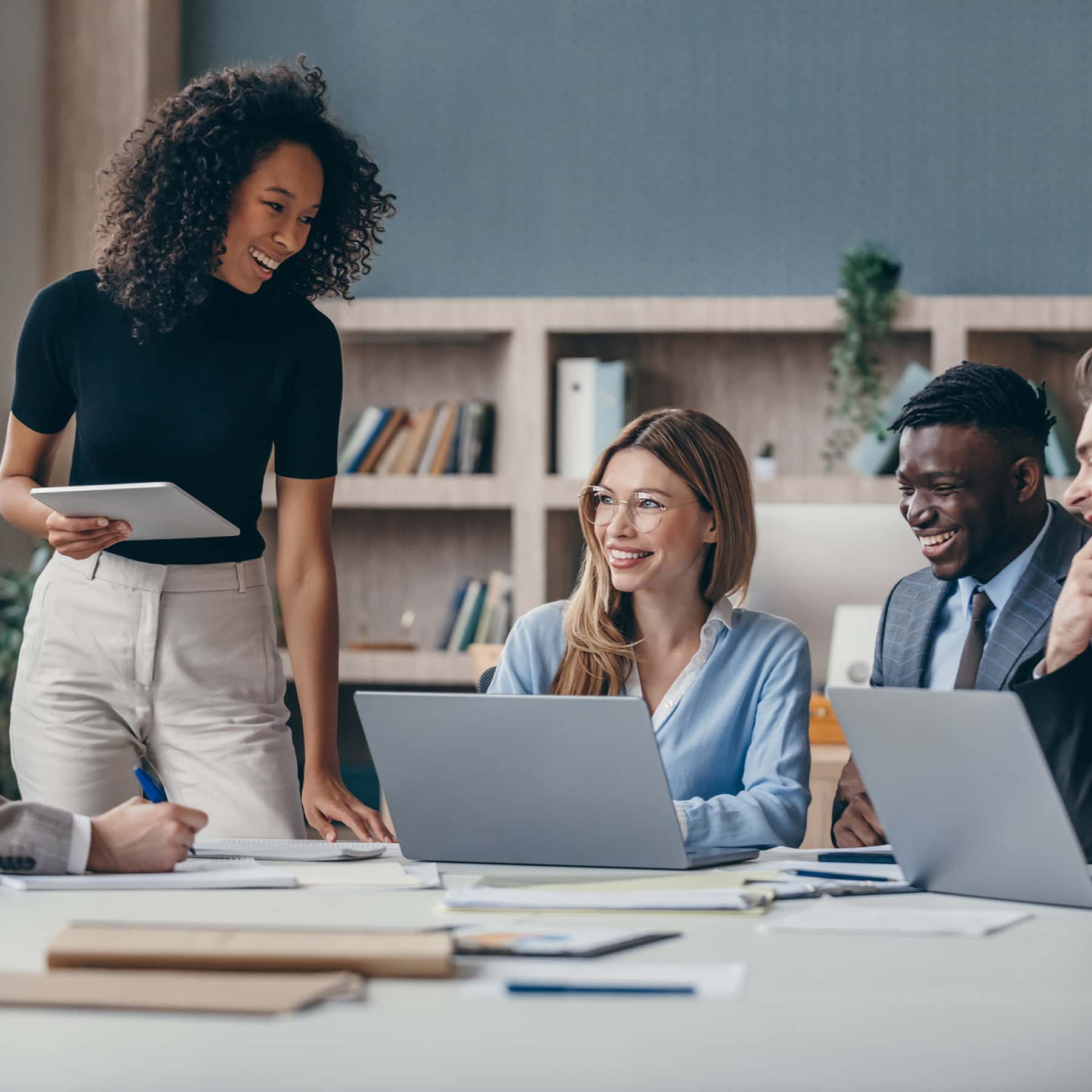Three diverse team members at big table with laptops. All three are smiling.