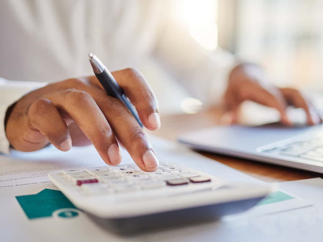 Close up of hand, calculator, and computer paying bills. 