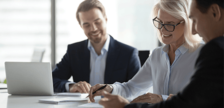 Three people smiling and discussing printed documents in an office meeting room